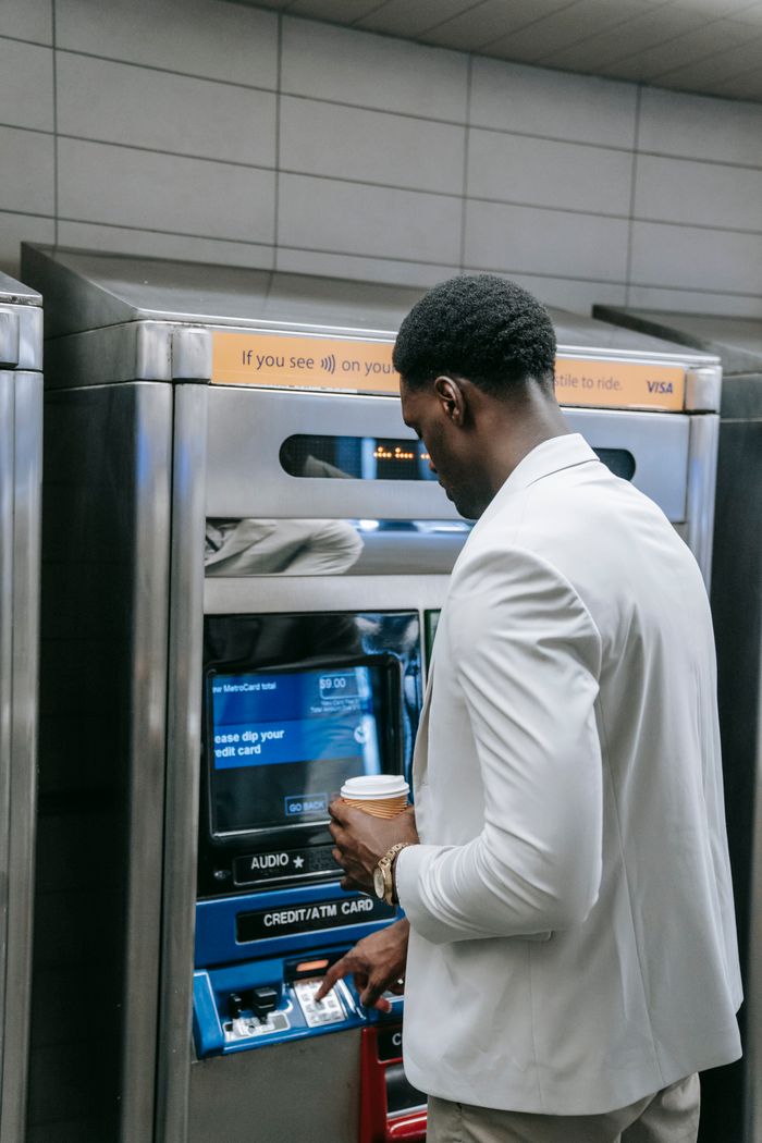 Businessman with coffee uses ATM indoors. Finance and transactions made simple.